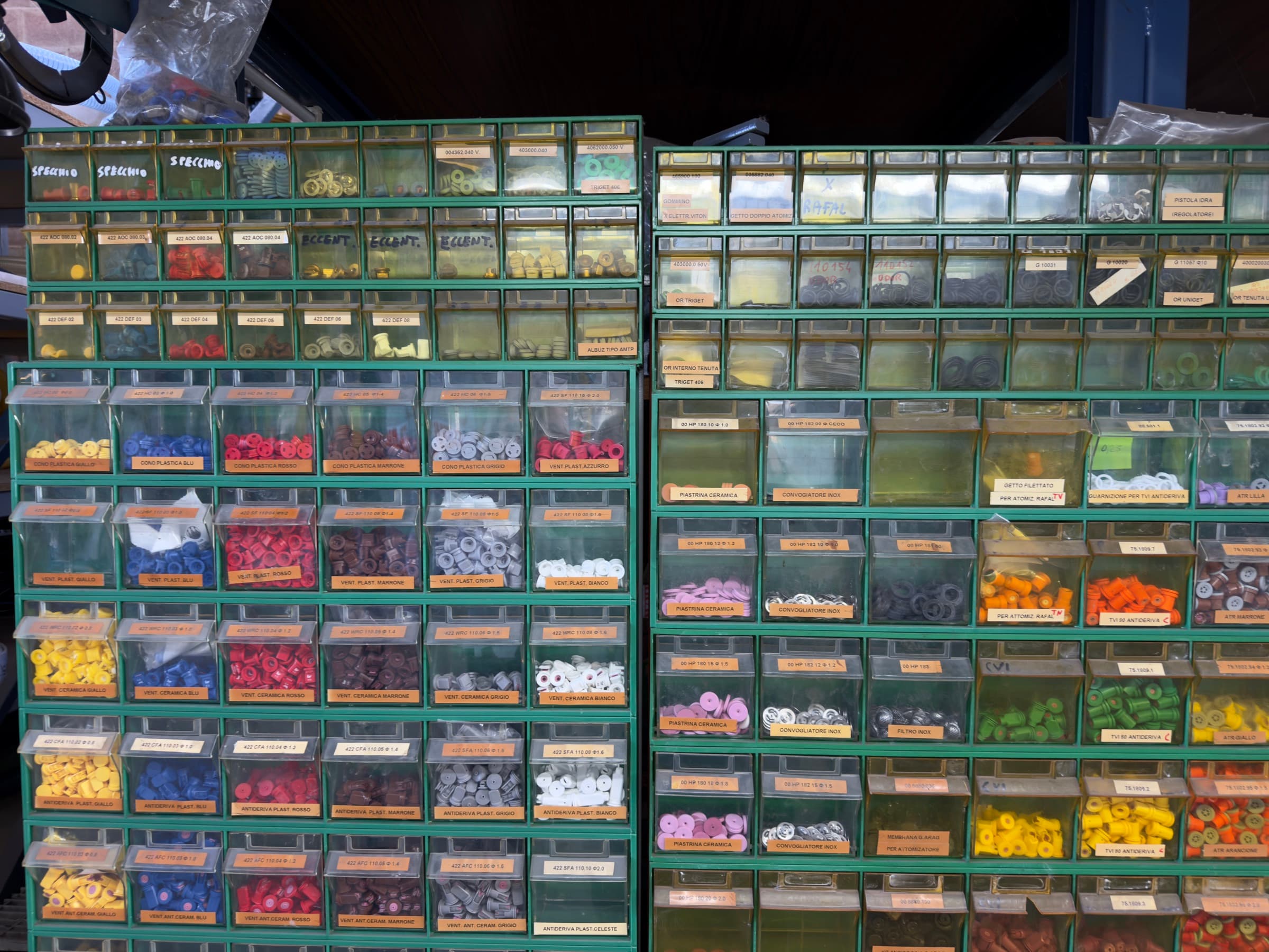 Cassettiere verdi con ugelli divisi per colore, gialli, blu, rossi, marroni, grigi e bianchi, e in alto cassetti più piccoli di minuteria etichettata