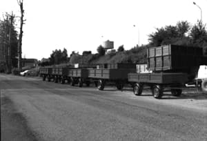 Foto d'epoca in bianco e nero: rimorchi agricoli a sponde alte esposti in fila lungo la strada alla vecchia sede Claut